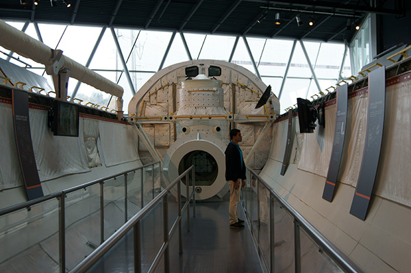 A young man stands in the cargo bay of the space shuttle full fuselage trainer at the museum of flight in Seattle. Despite being tall he is dwarfed.